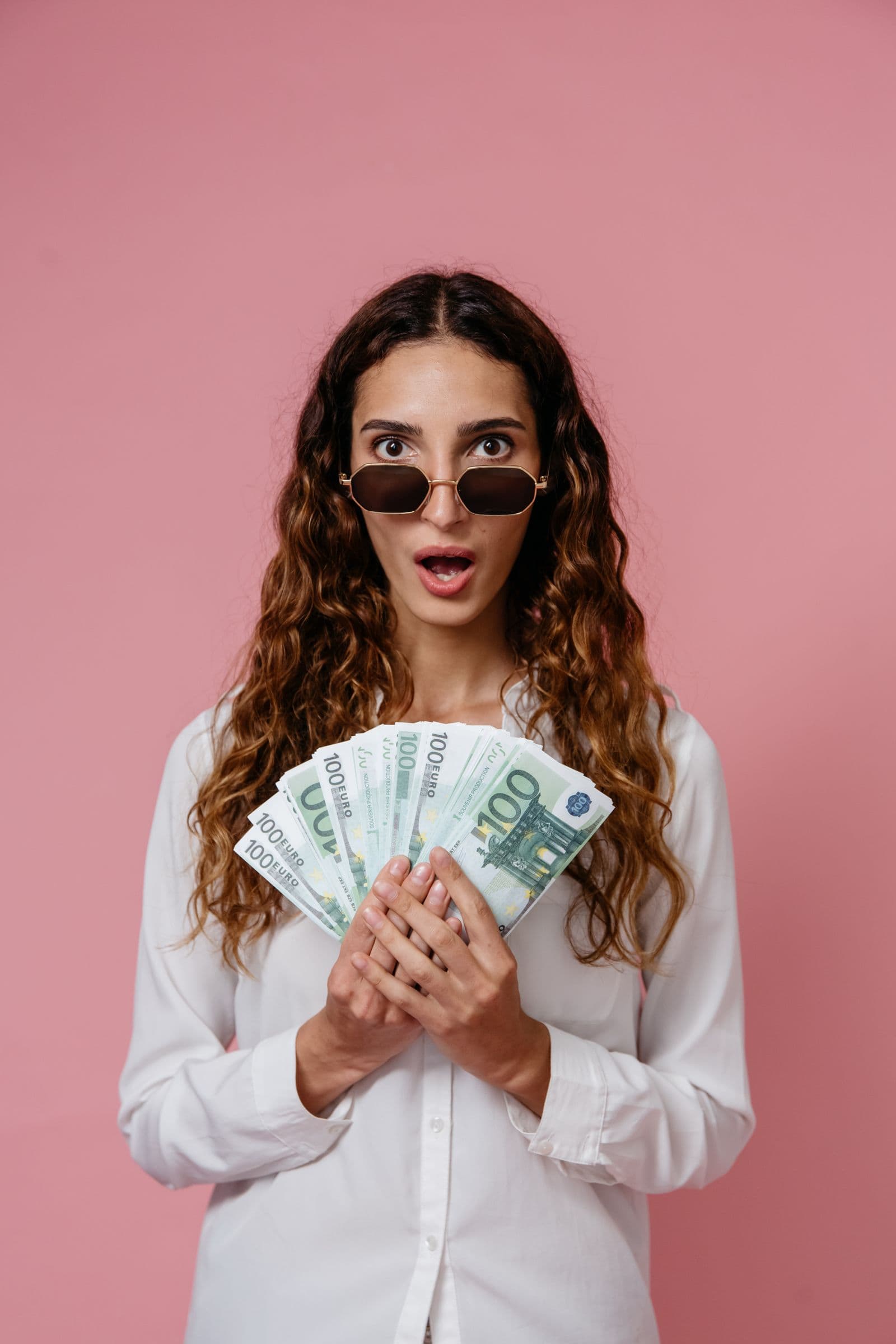 Une jeune femme tient des billets en euros avec une expression enthousiaste
